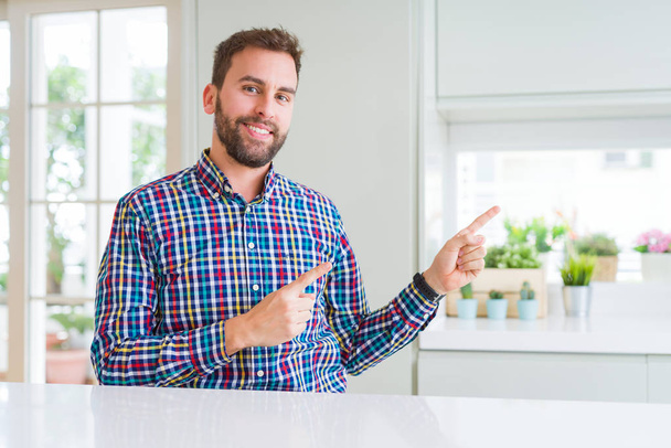 Przystojny mężczyzna noszenia uśmiechający się kolorowy koszula i patrząc na kamery, wskazując z dwóch rąk i palców na bok. - Zdjęcie, obraz