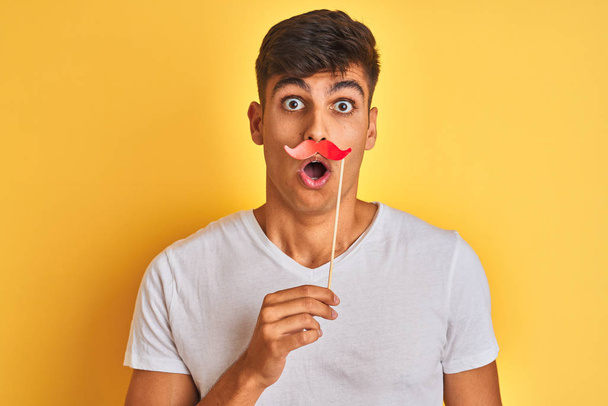 Jeune homme indien tenant moustache fanny debout sur fond jaune isolé effrayé en état de choc avec un visage surprise, effrayé et excité par l'expression de la peur
 - Photo, image