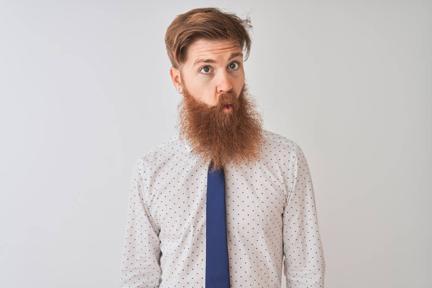Young redhead irish businessman standing over isolated white background making fish face with lips, crazy and comical gesture. Funny expression. - Photo, Image