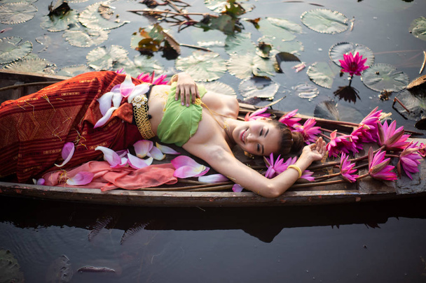 Draufsicht Frau in traditioneller Kleidung liegt neben rosa Lotus im Boot am See - Foto, Bild