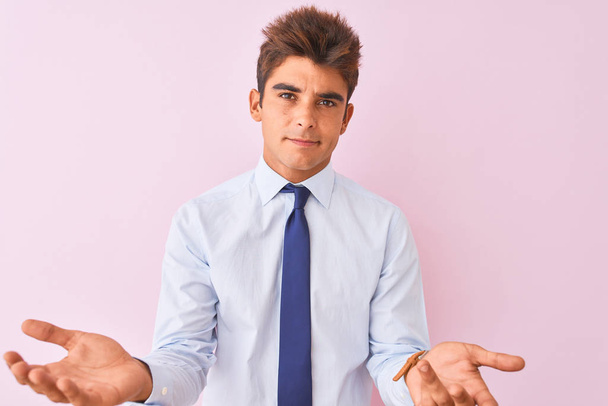 Young handsome businessman wearing shirt and tie standing over isolated pink background clueless and confused with open arms, no idea concept. - Photo, Image