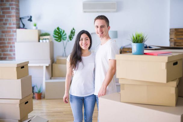 Νεαρό όμορφο ζευγάρι στέκεται στο νέο σπίτι γύρω από κουτιά από χαρτόνι - Φωτογραφία, εικόνα