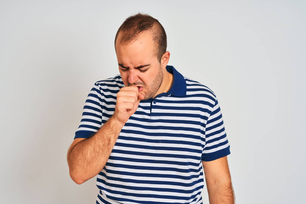 Young man wearing casual striped polo standing over isolated white background feeling unwell and coughing as symptom for cold or bronchitis. Healthcare concept. - Photo, Image