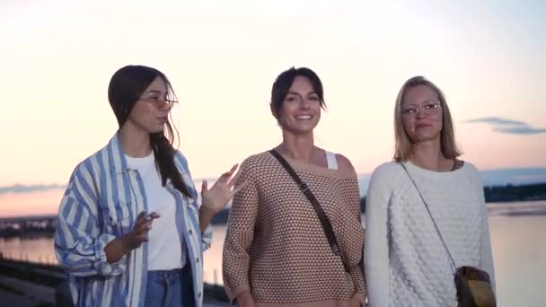 Trzy kobiety rozmawiają i śmieją się na zewnątrz o zachodzie słońca. - Materiał filmowy, wideo