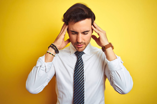 Young handsome businessman wearing elegant shirt and tie over isolated yellow background with hand on head for pain in head because stress. Suffering migraine. - Photo, Image