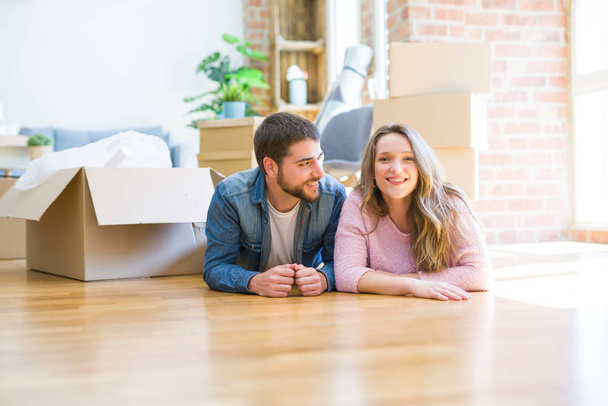 Jong mooi paar in liefde ontspannen liggend op de vloer samen met kartonnen dozen rond voor verhuizen naar een nieuw huis - Foto, afbeelding