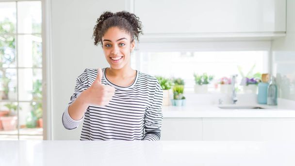 Красива афроамериканець жінка з афро волосся носити випадковий смугастий светр робити щасливі пальці вгору жест з рук. Затвердження виразу дивлячись на камеру, що показує успіх. - Фото, зображення