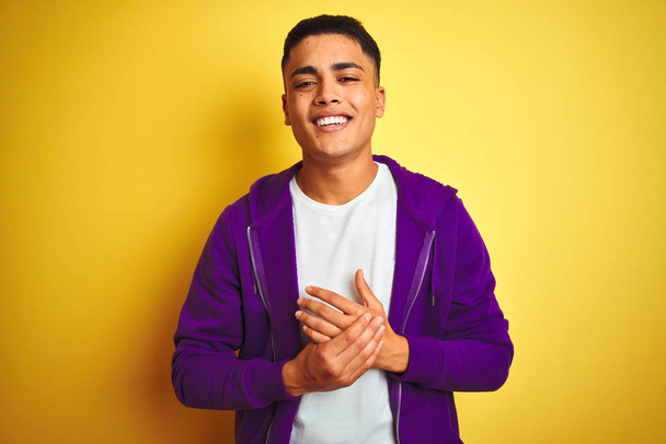 孤立した黄色の背景の上に立つ紫色のスウェットシャツを着た若いブラジル人男性は、手を合わせて指を組み、リラックスして陽気な笑顔を浮かべていました。成功と楽観的 - 写真・画像