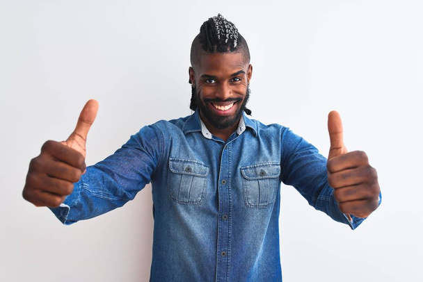 Afro-Amerikaanse man met vlechten dragen denim shirt over geïsoleerde witte achtergrond goedkeuren doen positieve gebaar met de hand, duimen omhoog glimlachend en blij voor succes. Winnaar gebaar. - Foto, afbeelding