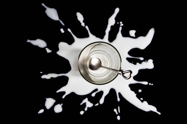Vaso de cristal vacio sobre una mancha de leche en fondo negro - Foto, Imagen