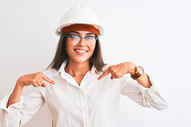 Молодая красивая архитектор женщина в шлеме и очках на изолированном белом фоне выглядит уверенно с улыбкой на лице, указывая на себя пальцами гордый и счастливый
. - Фото, изображение