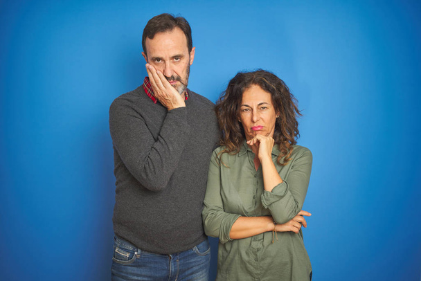 Beautiful middle age couple together standing over isolated blue background thinking looking tired and bored with depression problems with crossed arms. - Fotoğraf, Görsel