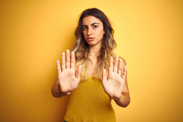 Mladá krásná žena nosí tričko přes žlutý izolovaný podklad odstěhovat ruce dlaně ukazující odmítnutí a popírání se strachu a nechutným výrazem. Zastavení a zákaz. - Fotografie, Obrázek
