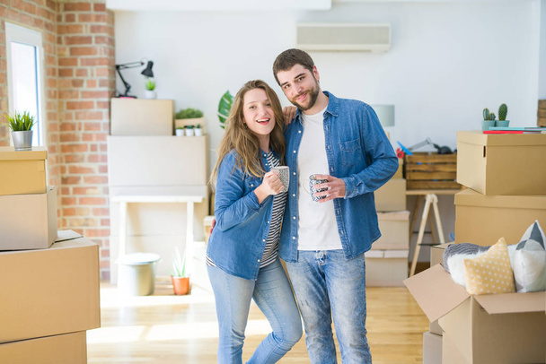 Молодая пара отдыхает от переезда в новый дом, пьет кофе вокруг картонных коробок
 - Фото, изображение