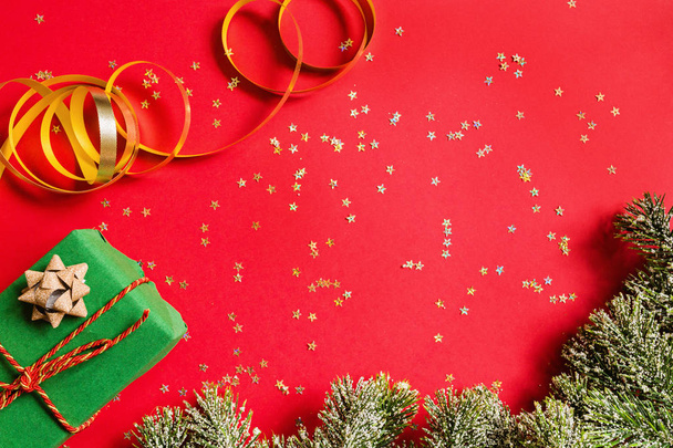 Christmas gift, tree branches on red background with golden confetti. new year concept. Greeting card, xmas celebration 2020. Flat lay, top view, copy space, mockup - Foto, Imagem