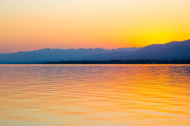 Nádherný západ slunce na jezeře v horách. Kyrgyzstán, jezero Issyk-kule. Světlá obloha, pozadí v teplých barvách. - Fotografie, Obrázek