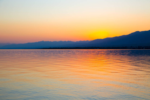 Nádherný západ slunce na jezeře v horách. Kyrgyzstán, jezero Issyk-kule. Světlá obloha, pozadí v teplých barvách. - Fotografie, Obrázek