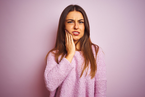 Mujer hermosa joven con suéter casual de pie sobre fondo rosa aislado tocando la boca con la mano con expresión dolorosa debido a dolor de muelas o enfermedad dental en los dientes. Concepto de dentista
. - Foto, imagen