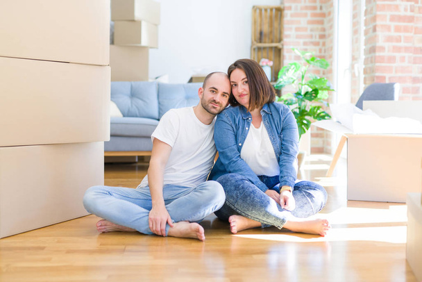 床の上に座っている若いカップルは、真剣な表情で新しい家に移動する段ボール箱。カメラを見てシンプルで自然な. - 写真・画像