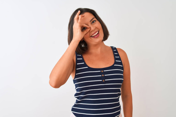 Young beautiful woman wearing blue striped t-shirt standing over isolated white background doing ok gesture with hand smiling, eye looking through fingers with happy face. - Photo, Image