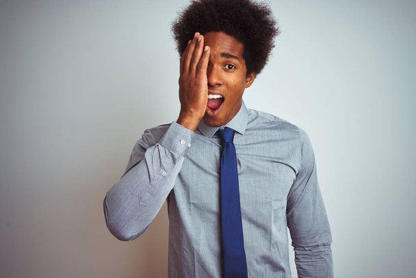 American business man with afro hair wearing shirt and tie over isolated white background covering one eye with hand, confident smile on face and surprise emotion. - Φωτογραφία, εικόνα