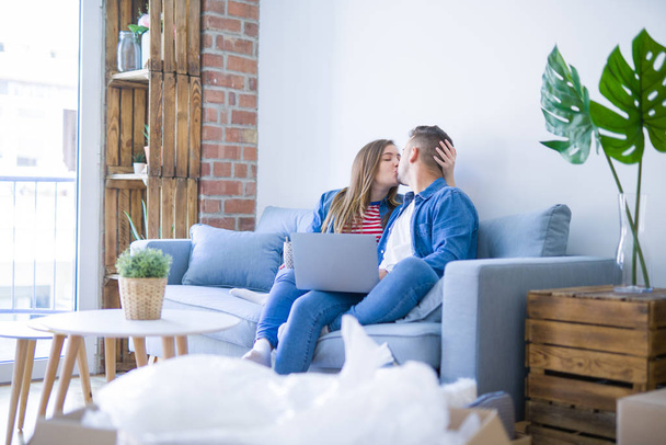 Malý manželský pár, který sedí na pohovce a používá počítačový notebook kolem lepenkových krabic, velmi šťastný přesun do nového domu - Fotografie, Obrázek