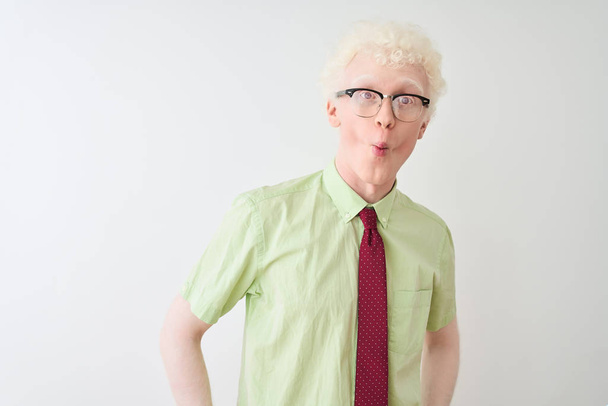 Young albino businessman wearing shirt and tie standing over isolated white background making fish face with lips, crazy and comical gesture. Funny expression. - Fotó, kép