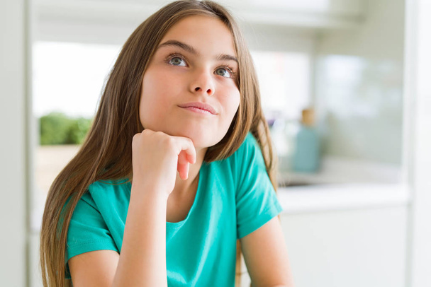 Beautiful young girl kid wearing green t-shirt with hand on chin thinking about question, pensive expression. Smiling with thoughtful face. Doubt concept. - Foto, immagini