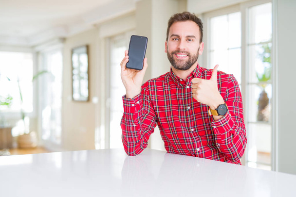 Komea mies näyttää älypuhelimen näytön onnellinen iso hymy tekee ok merkki, peukalo ylös sormilla, erinomainen merkki
 - Valokuva, kuva