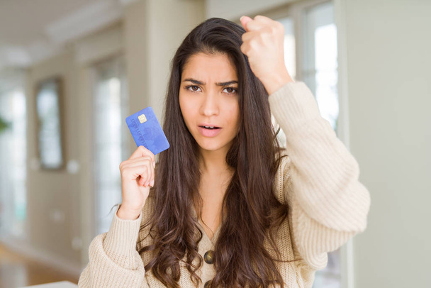 Mujer joven sosteniendo tarjeta de crédito como pago molesto y frustrado gritando con ira, loco y gritando con la mano levantada, concepto de ira
 - Foto, Imagen