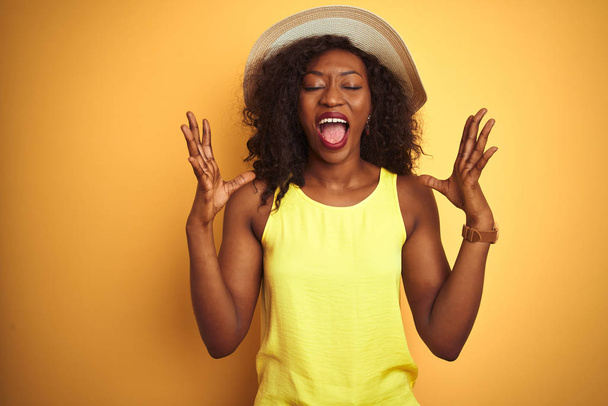 Jeune femme afro-américaine portant t-shirt et chapeau sur fond jaune isolé célébrant fou et fou de succès avec les bras levés et les yeux fermés hurlant excités. Concept gagnant
 - Photo, image