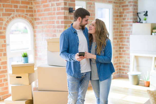 Young couple moving to a new house using smartphone around cardboard boxes - Foto, imagen