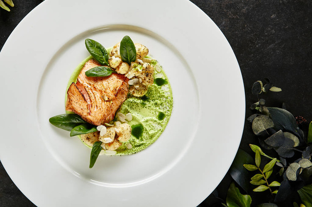 Exquisite Serving White Restaurant Plate with Fillet of Salmon 48 Degrees, Green Peas Cream and Burnt Cauliflower Top View. Stylish Italian Seafood Dish on Natural Black Marble Background - Foto, imagen