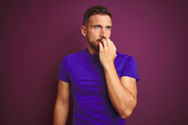 Der junge Mann trägt ein lässiges lila T-Shirt über fliederfarbenem Hintergrund und sieht gestresst und nervös aus, die Hände auf den Mund beißenden Nägeln. Angstproblem. - Foto, Bild