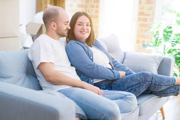 Νεαρό ζευγάρι στην αγάπη χαλάρωση και αγκάλιασμα κάθεται στον καναπέ στο νέο σπίτι, χαμογελαστός πολύ χαρούμενος για τη μετακίνηση σε ένα νέο διαμέρισμα - Φωτογραφία, εικόνα