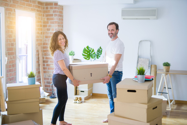 Middle age senior couple moving to a new house, holding cardboard boxing smiling happy in love with apartmant - Fotoğraf, Görsel