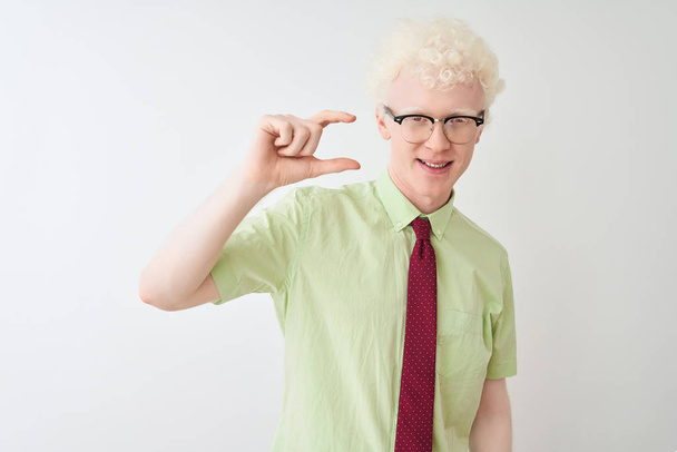 Genç albino işadamı gömlek giyen ve izole beyaz arka plan üzerinde duran kravat gülümseyerek ve emin el parmakları görünümlü ve kamera ile küçük boyutlu işareti yapıyor gesturing. Ölçü kavramı. - Fotoğraf, Görsel