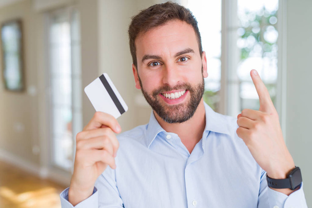 Yakışıklı iş adamı kredi kartı tutan mutlu yüz, bir numaralı ile bir fikir ya da soru işaret parmağı ile şaşırttı - Fotoğraf, Görsel