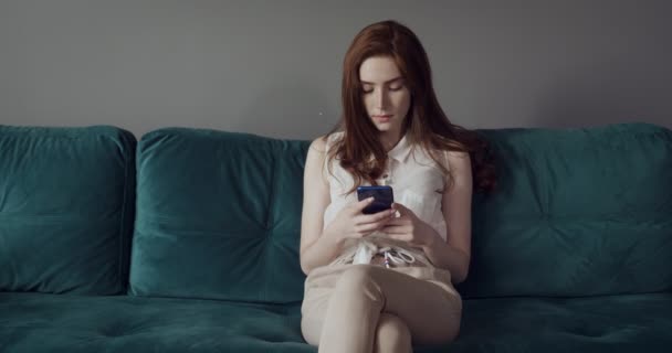 Young woman sits on the couch and using smartphone. - Metraje, vídeo