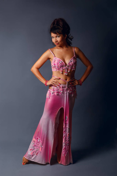 Belly dancer performing belly dance in the ethnic pink costume for dancing on gray background - 写真・画像
