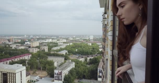 Jonge vrouw op zoek naar de stad vanuit het raam. - Video