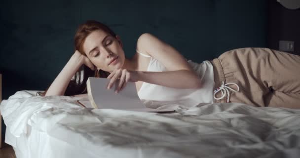 Redhead woman lying and relax on the bed and looks in her diary. - Πλάνα, βίντεο