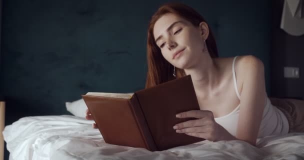 Rudowłosa kobieta leży i relaksuje się na łóżku i zagląda do pamiętnika. - Materiał filmowy, wideo