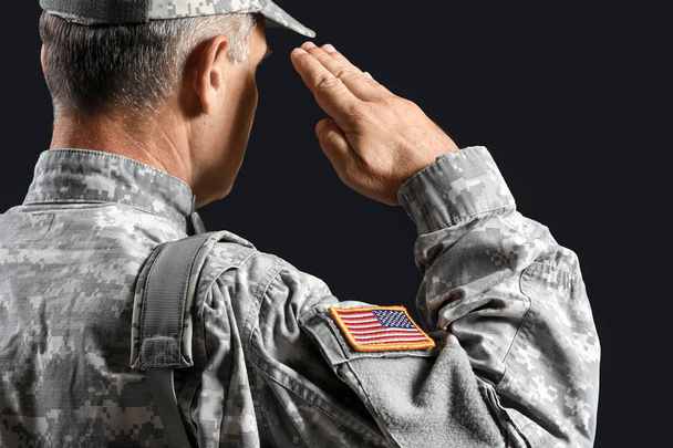 Saluting mannelijke soldaat op donkere achtergrond - Foto, afbeelding