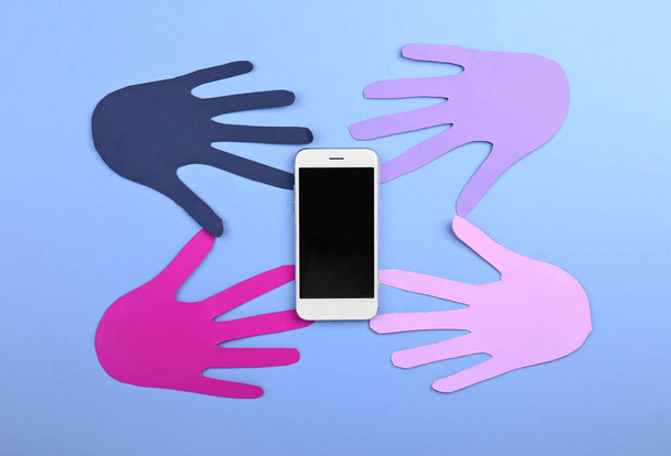 Teléfono móvil moderno con palmas humanas de papel sobre fondo de color
 - Foto, Imagen