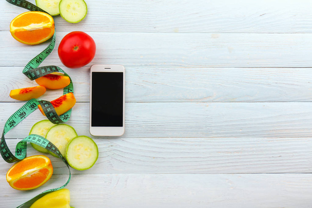 Modern mobile phone with fresh fruits, vegetables and measuring tape on wooden background - Photo, image