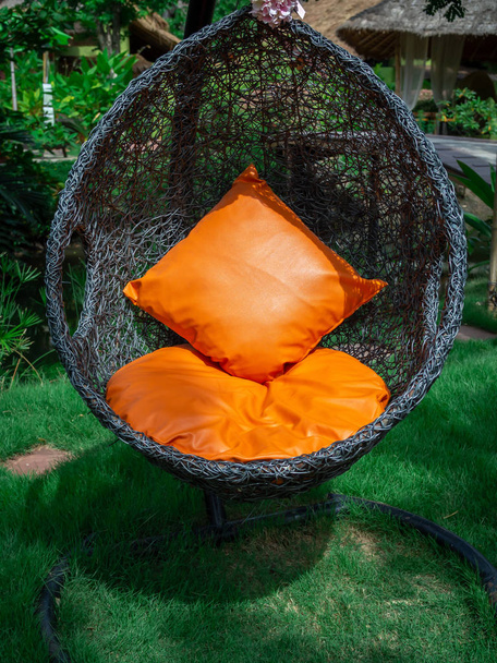 オレンジ色の枕と卵椅子をぶら下げるラタンラウンジャー. - 写真・画像