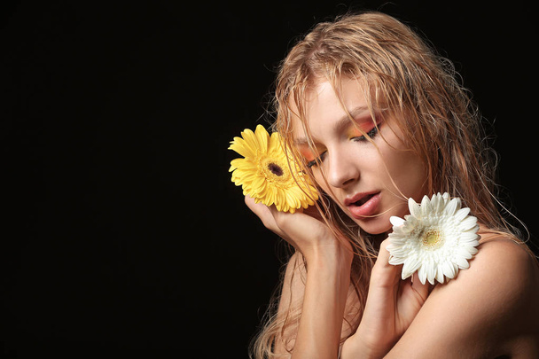 Beautiful sexy young woman with gerbera flowers on dark background - Foto, Imagem