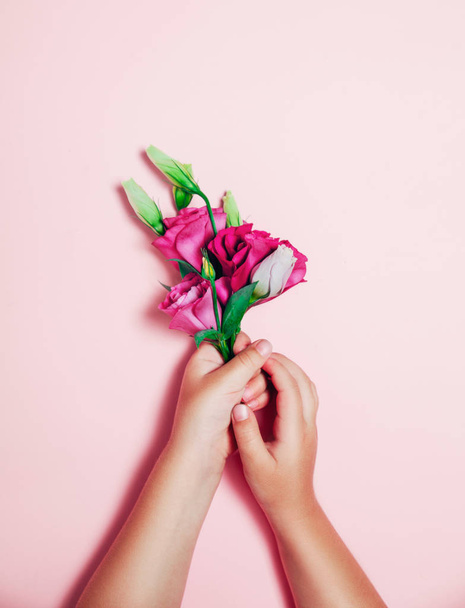 Little children hands holding beautiful flowers on pink background. - Photo, Image