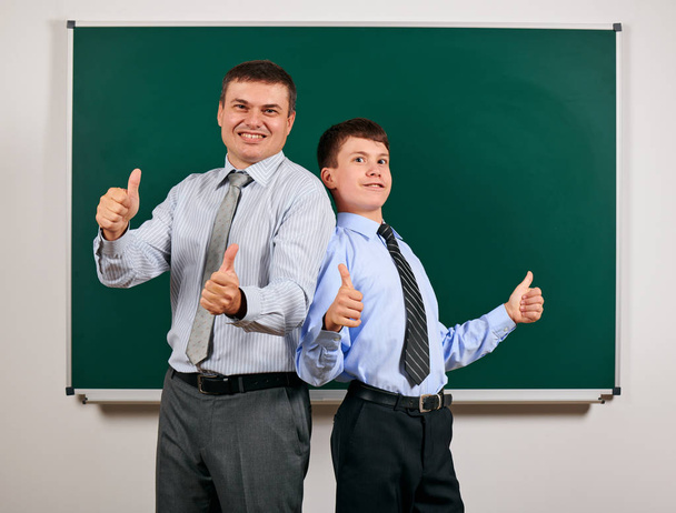 Πορτρέτο ενός άντρα και αγόρι ντυμένος σε μια επιχειρηματική κοστούμια κοντά στο φόντο μαυροπίνακα, δείχνουν καλύτερη χειρονομία-μάθηση και την εκπαίδευση έννοια - Φωτογραφία, εικόνα
